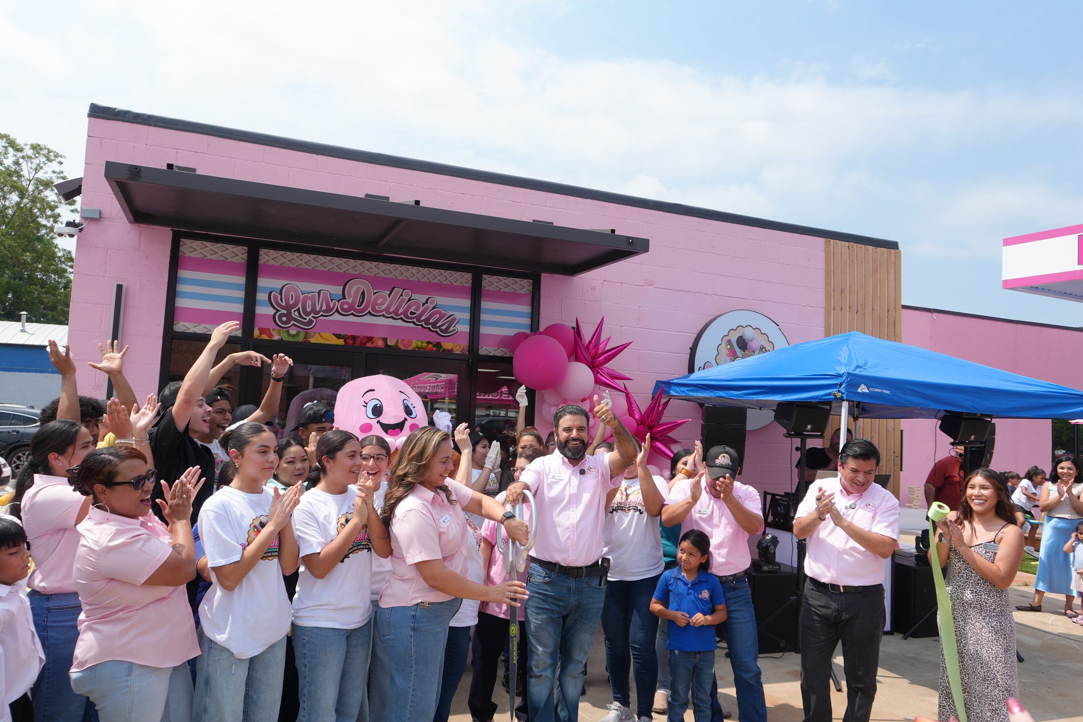 The family and team cutting the ribbon outside the pink Harkrider Street shop, with the pink ice cream mascot behind them